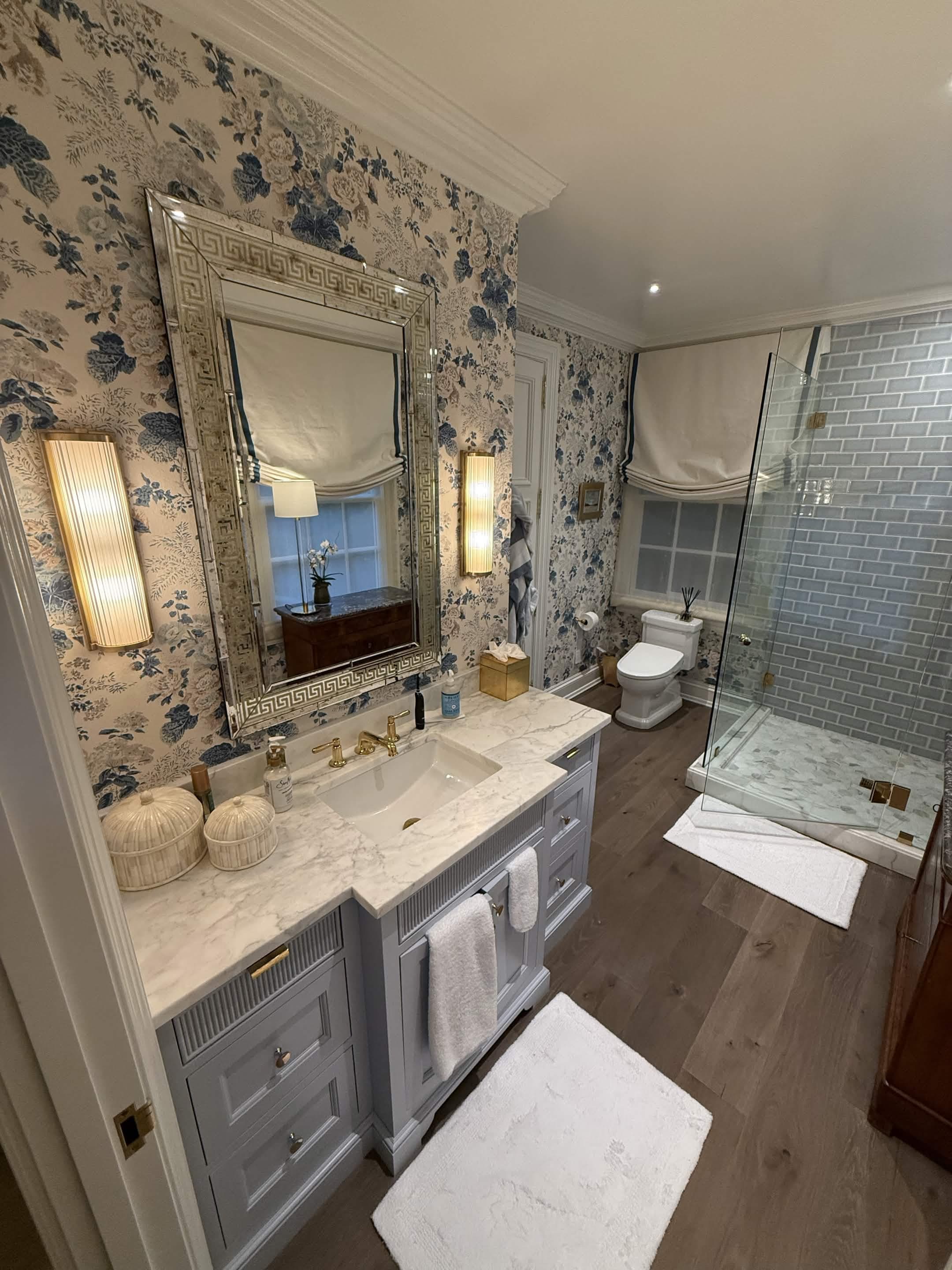 A powder bath with blue floral wallpaper, a marble vanity, and a glass shower