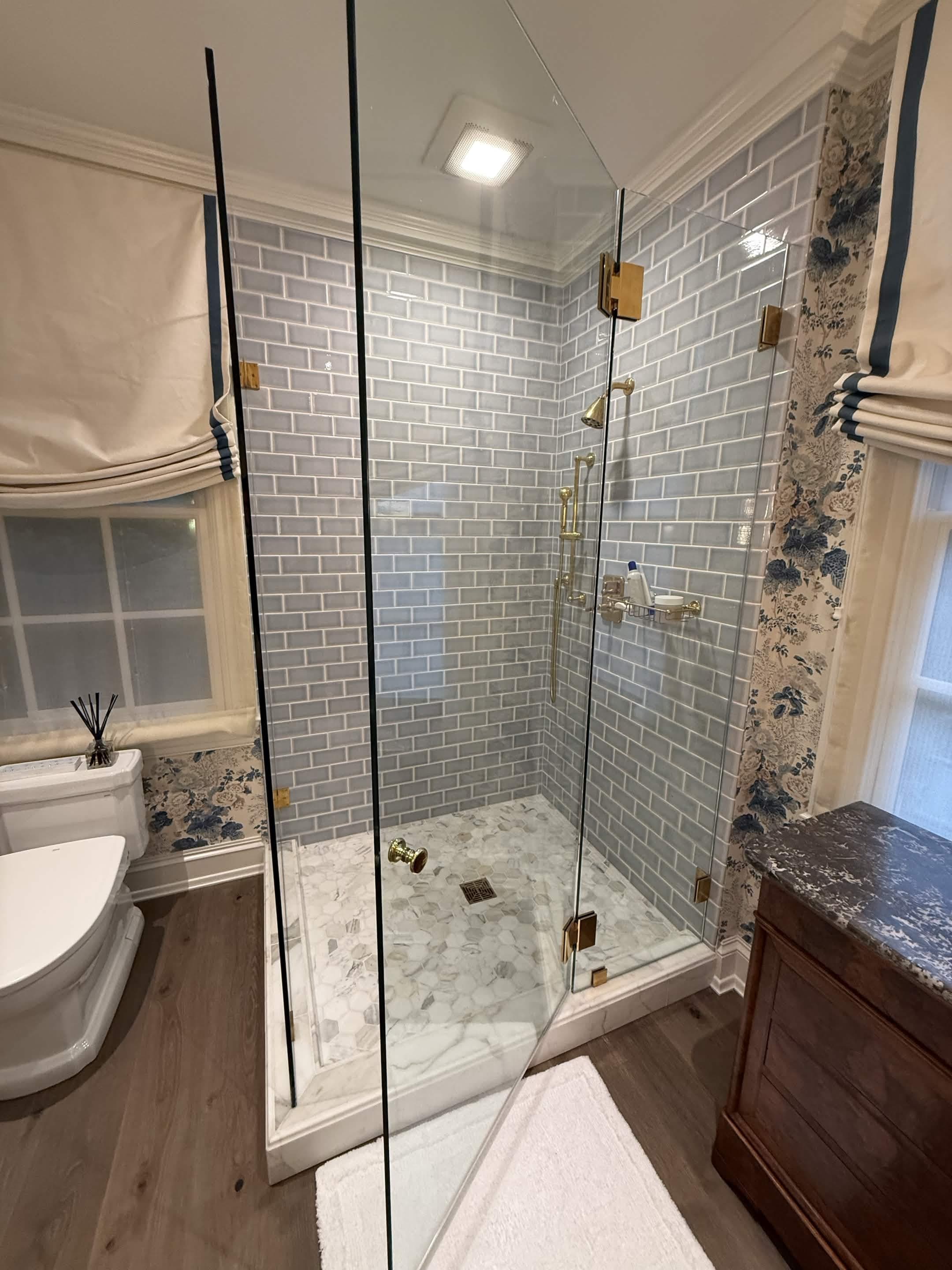 A spa ensuite with a frameless glass shower, grey subway tile, and brass fittings